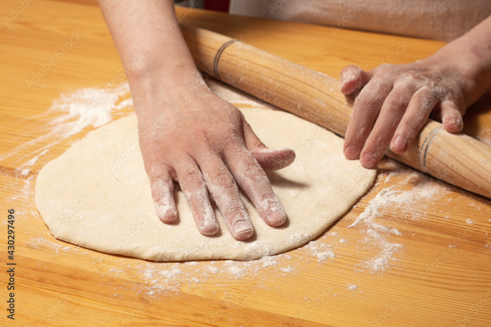 Hands with rolling-pin make dough for pizza. Italian pizza cooking preparation process on wood table. Pizza dough