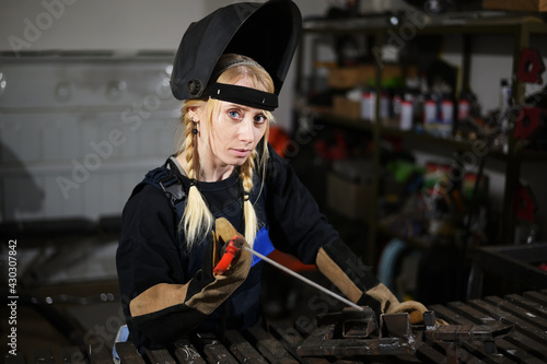 Portrait of cute caucasian blonde girl welder working in a mask in the garage