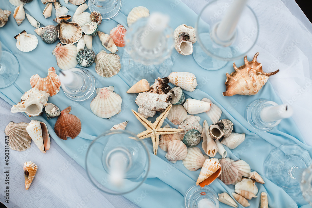 Fototapeta premium Stylish design of the wedding table in a nautical style. The decor is made of candles, shells and starfish with a blue fabric close-up. Marine style for a photo shoot