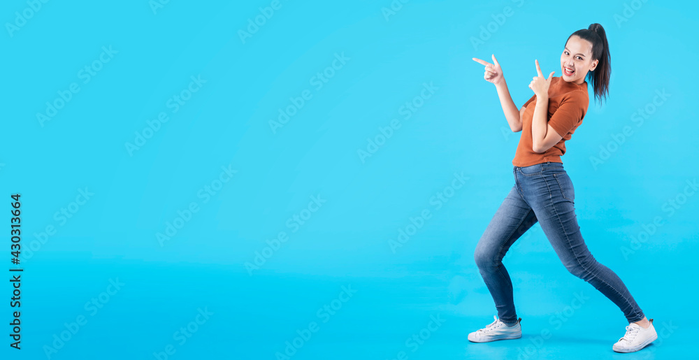 Cheerful Asian female girl indicate thumb empty space hand gesture finger point wide smile open mouth wear casual cloth jeans isolated blue color background