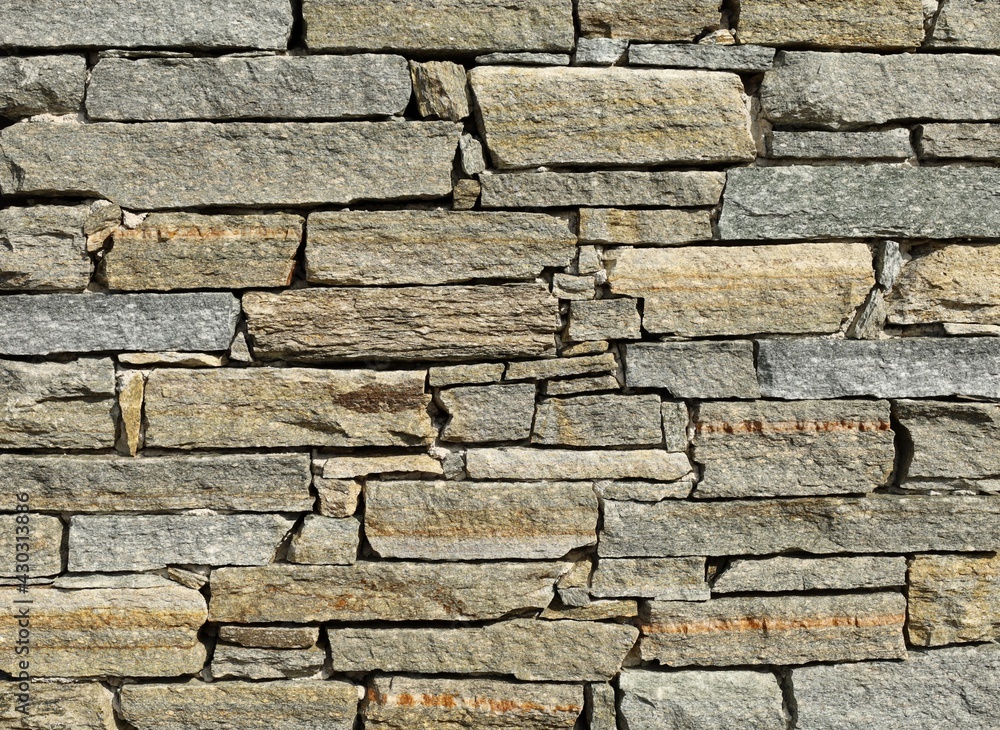Fototapeta premium Stone wall made of horizontal shaped natural rocks. The colors are gray, brown and green with stripes of different colors. Masonry. Background and texture