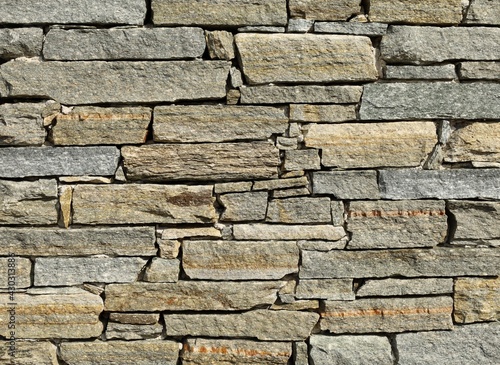 Stone wall made of horizontal shaped  natural rocks. The colors are gray  brown and green with stripes of different colors. Masonry. Background and texture