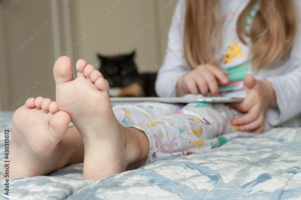 Girl in pajamas sits on the bed and plays on the tablet Girl in pajamas sits on the bed and plays on the tablet