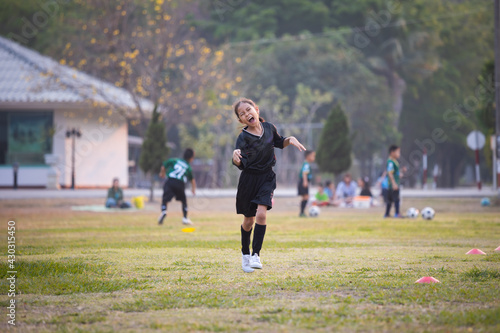 Asian child girl making funny face and running with happiness in the soccer field. Child is happy after win in game. Kid sport recreation concept.