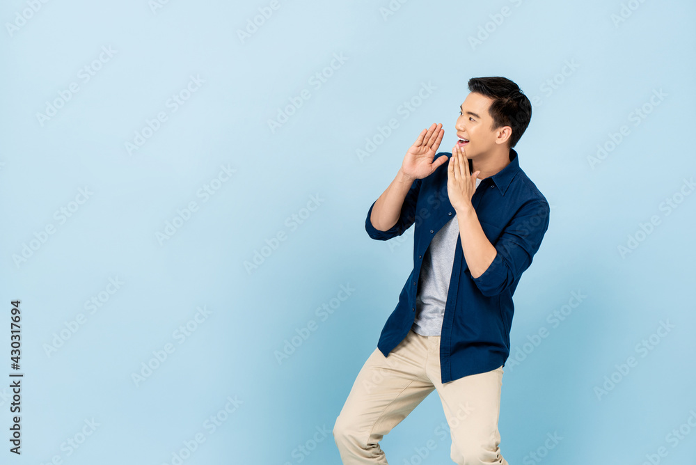 Young Asian man shouting and cupping hands around mouth in light blue isolated background with copy space Young Asian man shouting and cupping hands around mouth in light blue isolated background with copy space