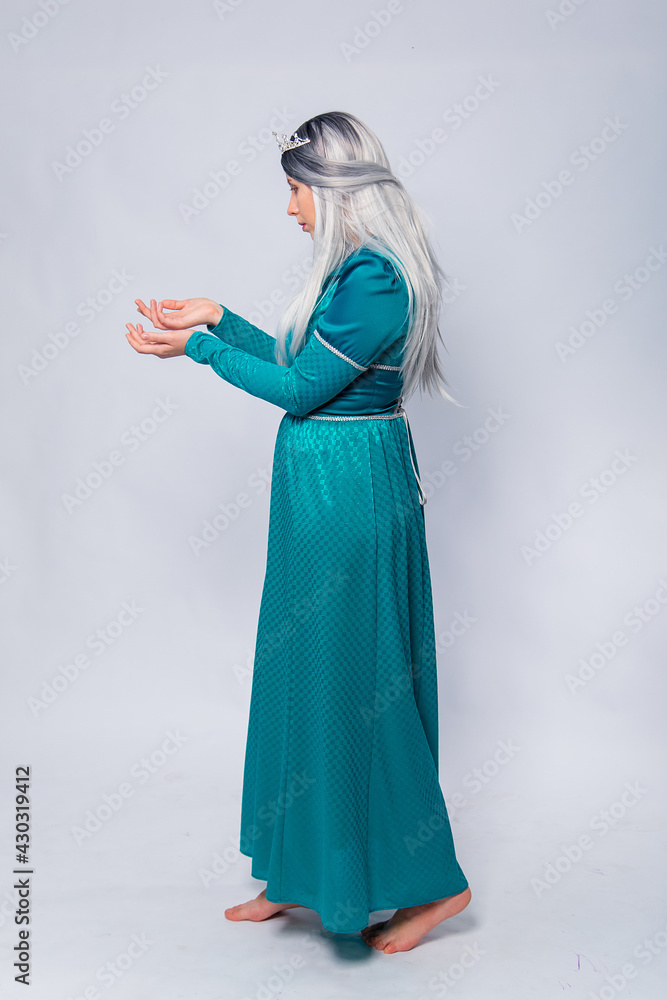 Naklejka premium Full length portrait of a princess in a medieval, fantasy, turquoise dress with ash hair and a silver crown, posing isolated on a white background. 