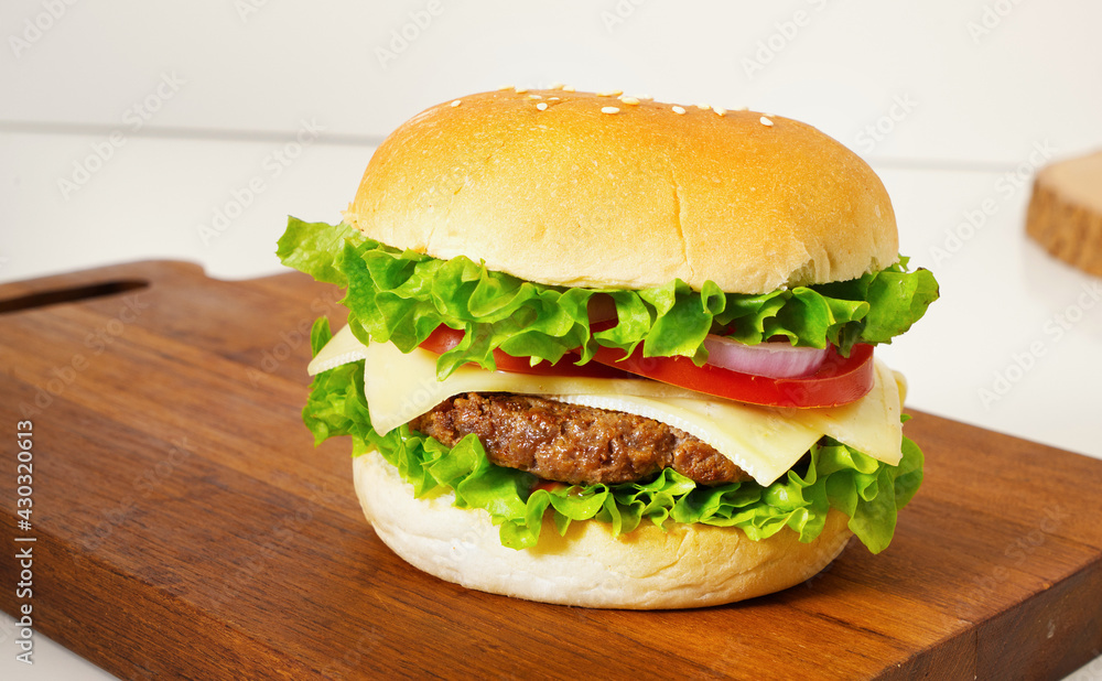 A close-up of a hamburger placed with lettuce, tomato, cheese, beef, onion on a wooden cutting board A close-up of a hamburger placed with lettuce, tomato, cheese, beef, onion on a wooden cutting board