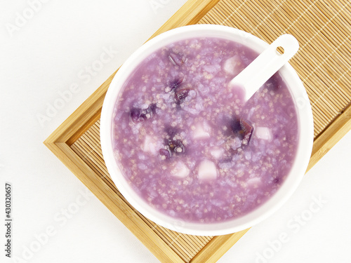 A bowl of purple sweet potato and millet porridge with a spoon on a tray, delicious diet, white background