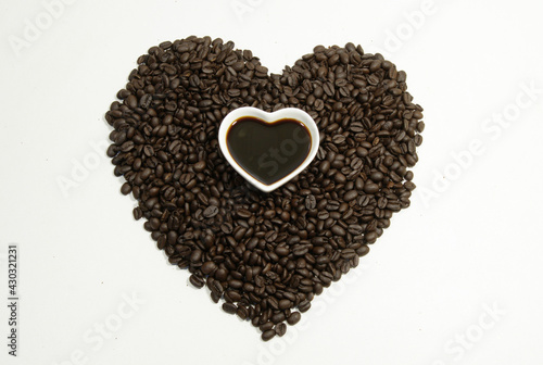 Black coffee beans are placed into a heart shape with a cup of heart-shaped coffee on, top view