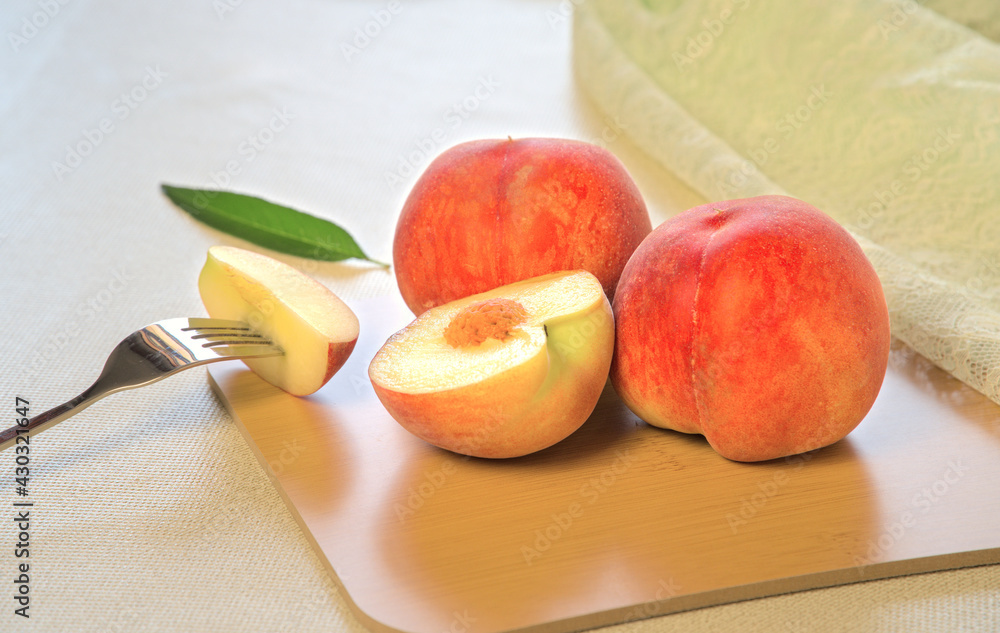 Two fresh peaches whole and a small piece cut on a fork, on wooden cutting board Two fresh peaches whole and a small piece cut on a fork, on wooden cutting board