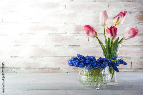 Foto Flowers of tulips and grape hyacinths in a jar and crystal glass on a rustical b