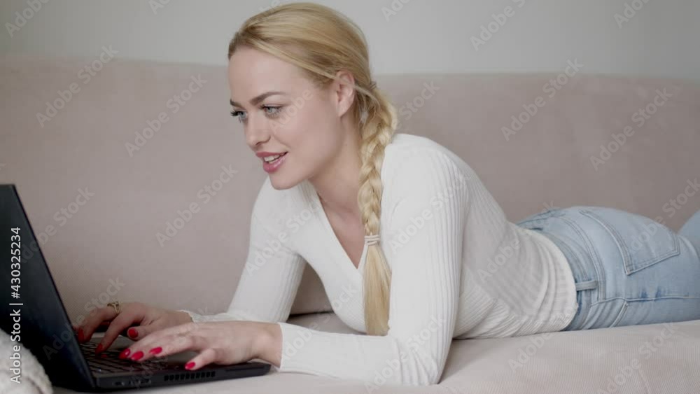 Blond female lying on sofa and browsing laptop Blond female lying on sofa and browsing laptop