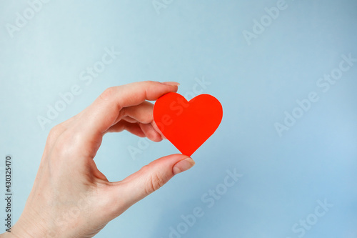 a woman's hand holds a red paper heart on a blue background, world blood donor Day, charity and care, blood donation