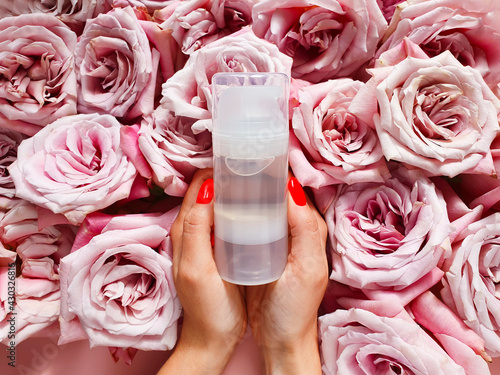 Transparent bottle of intimate lubricant gel, female hands with red nails and pink roses. Intimate massage and comfortable sex consept. Top view, mockup, template.
