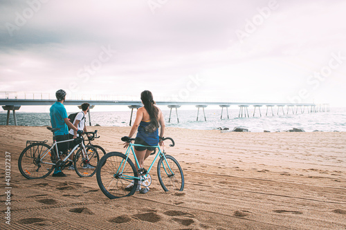 Canvas Print Friends seen from behind with their bikes on the beach at dawn looking out to sea