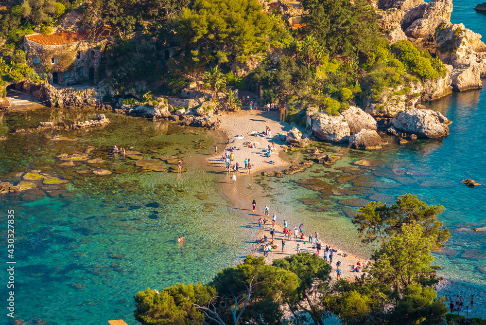 People walking on the a tiny stripe of sand among the sea, towards the entrance of Isola Bella Nature Reserve in Taormina, Sicily 