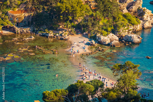 People walking on the a tiny stripe of sand among the sea, towards the entrance of Isola Bella Nature Reserve in Taormina, Sicily 