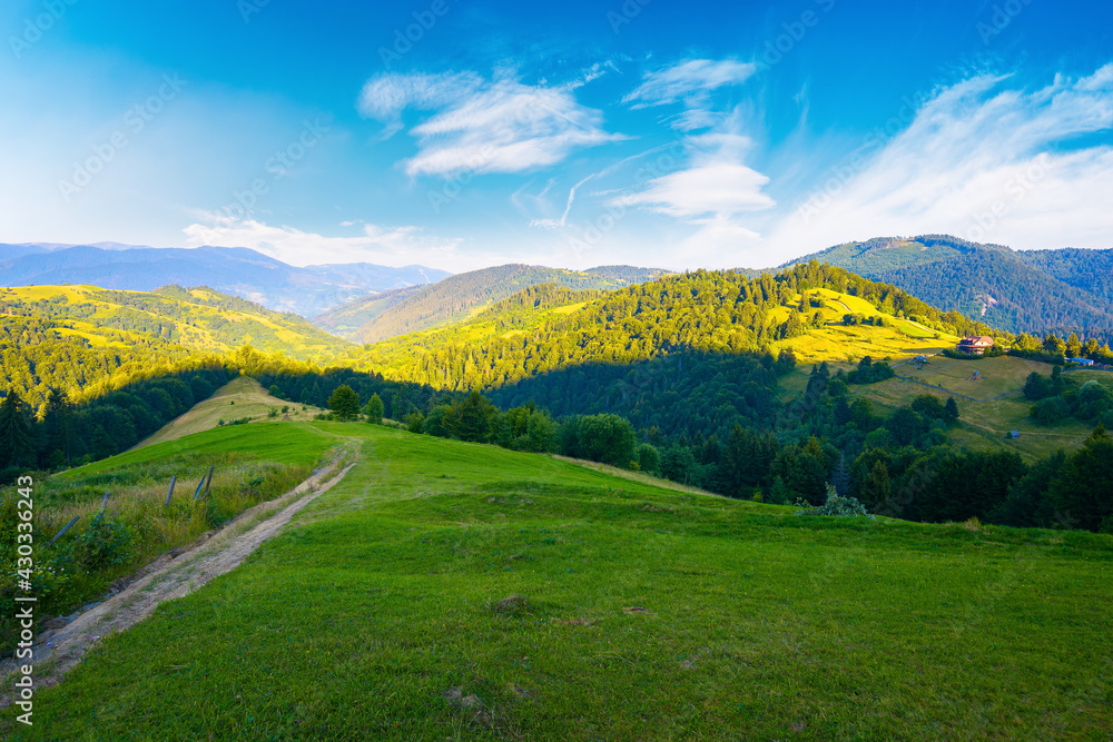 rural landscape in mountains at summer sunrise. country road through grassy pasture winding down in to the distant valley. clouds on the blue sky above the ridge in the distance
