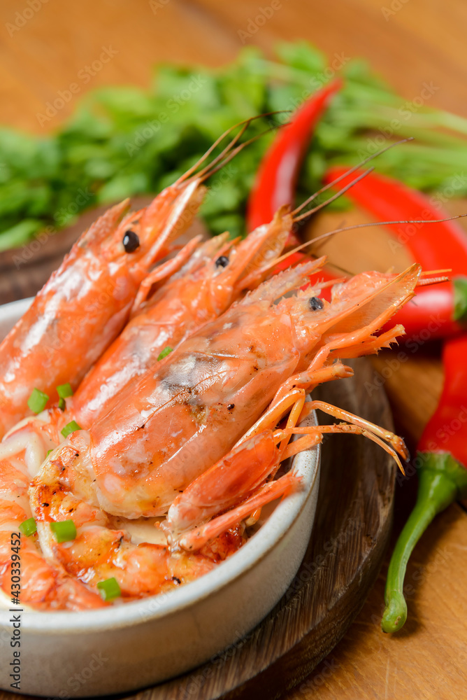 Cooked shrimps served in a white bowl on a wood plate with garlic onion and chili. Sea food. Cooked shrimps served in a white bowl on a wood plate with garlic onion and chili. Sea food.