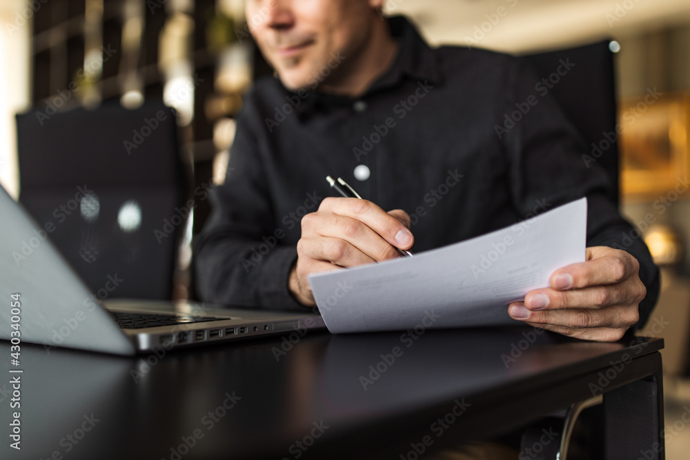 Close-up image of a man holding a pen and paper document and looking at laptop. Close-up image of a man holding a pen and paper document and looking at laptop.