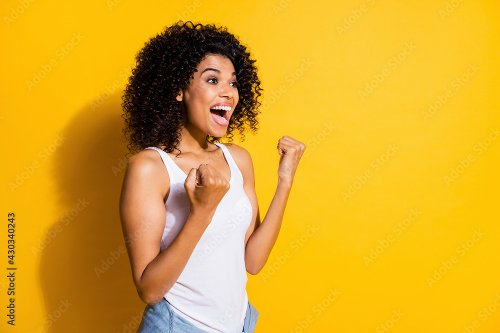 Photo of astonished young dark skin lady wear white singlet rising fists looking empty space isolated yellow color background Photo of astonished young dark skin lady wear white singlet rising fists looking empty space isolated yellow color background