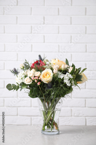 Beautiful bouquet with roses on grey table against white brick wall