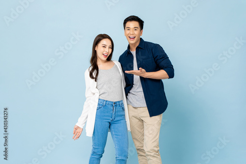 Foto Surprised smiling Asian couple in casual clothes standing in light blue isolated