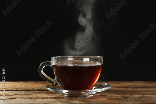 Cup with steam on wooden table against black background