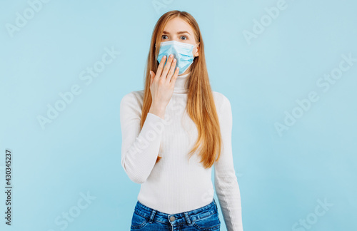 Excited young woman looking wide eyes at camera covering mouth with hands on isolated blue background