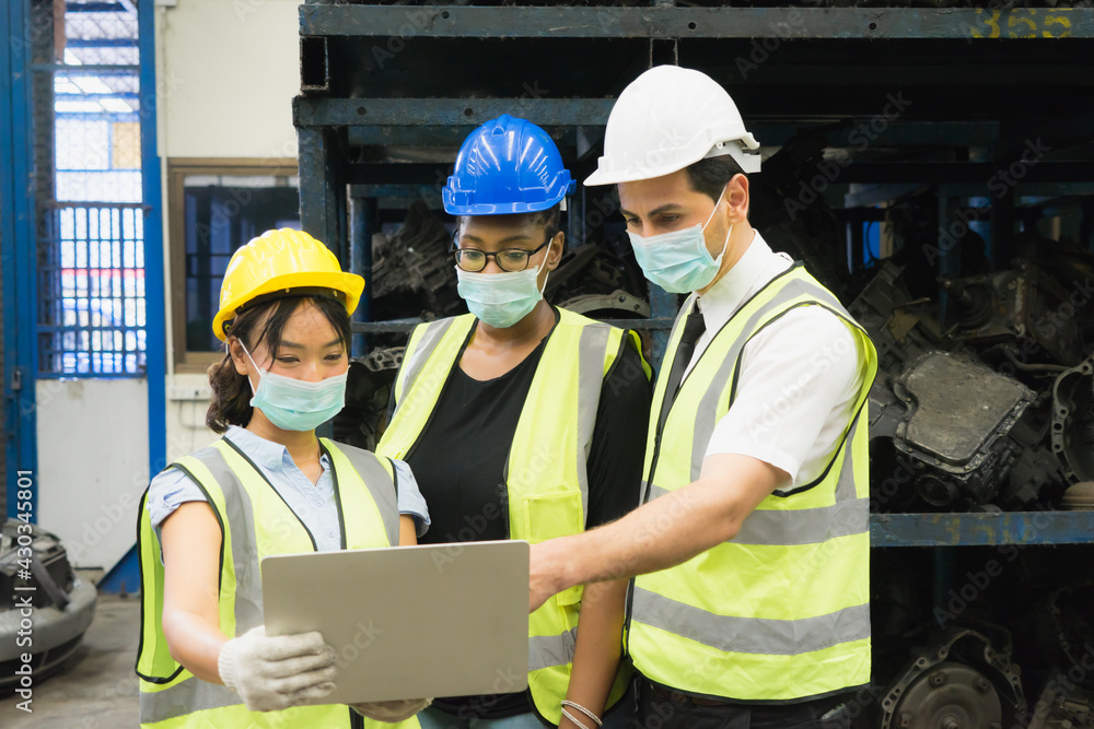Men and woman work together, wear safety facemask and using laptop. Caucasian engineer men, black woman, Asian woman wear facemask and using laptop in factory-warehouse Men and woman work together, wear safety facemask and using laptop. Caucasian engineer men, black woman, Asian woman wear facemask and using laptop in factory-warehouse