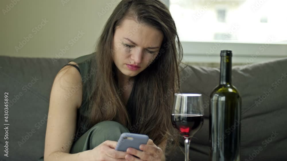 Crying woman is trying to call someone. She drinks wine alone. Pain, suffering, mental anguish. Crying woman is trying to call someone. She drinks wine alone. Pain, suffering, mental anguish.