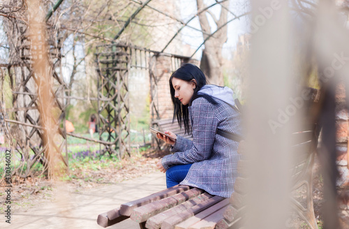 Portrait of beautiful brunette girl in plaid coat sits on a bench in the park