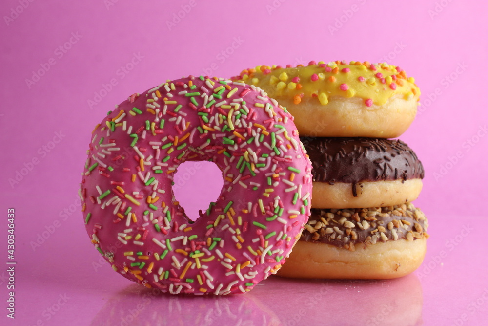 Sweet still life donut berliner close-up at the back lie a stack of three doughnut chocolate pink yellow on a bright pink fuchsia background with a place for text for a cafe for tablecloths for glue Sweet still life donut berliner close-up at the back lie a stack of three doughnut chocolate pink yellow on a bright pink fuchsia background with a place for text for a cafe for tablecloths for glue