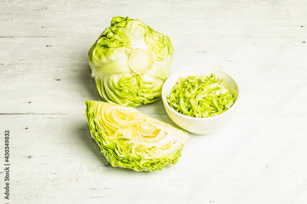 Obraz premium Fresh young shredded cabbage, whole head and cut piece on white wooden background