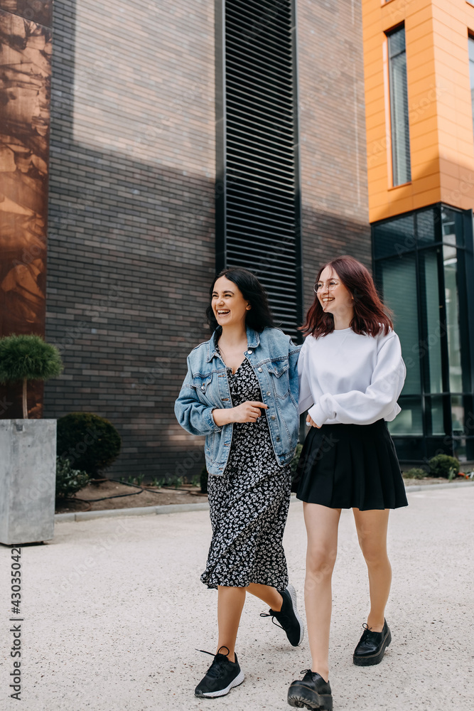 Two young women walking down the street, chatting and laughing. Best friends concept.