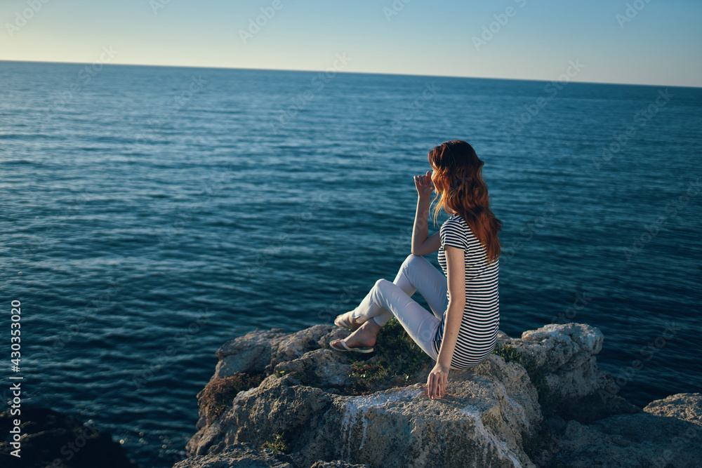 happy woman on a rock near the sea sunset blue sky and clear water