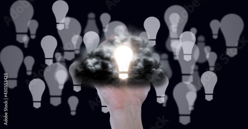 Composition of lit light bulb with cloud over hand and multiple light bulbs on black background