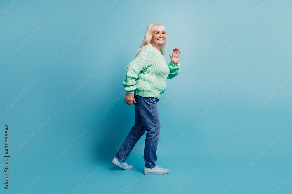 Candid old woman walk wave hand isolated over blue background Candid old woman walk wave hand isolated over blue background