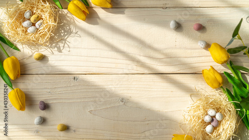 Canvas Print Spring Easter holiday top view flat white background with eggs in nests and yellow tulips on a light wooden table with natural sunlight
