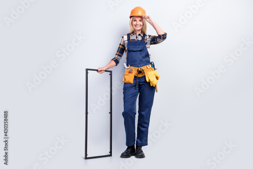 Photo of pretty cheerful age crafts lady dressed uniform arm helmet smiling holding metal frame isolated grey color background