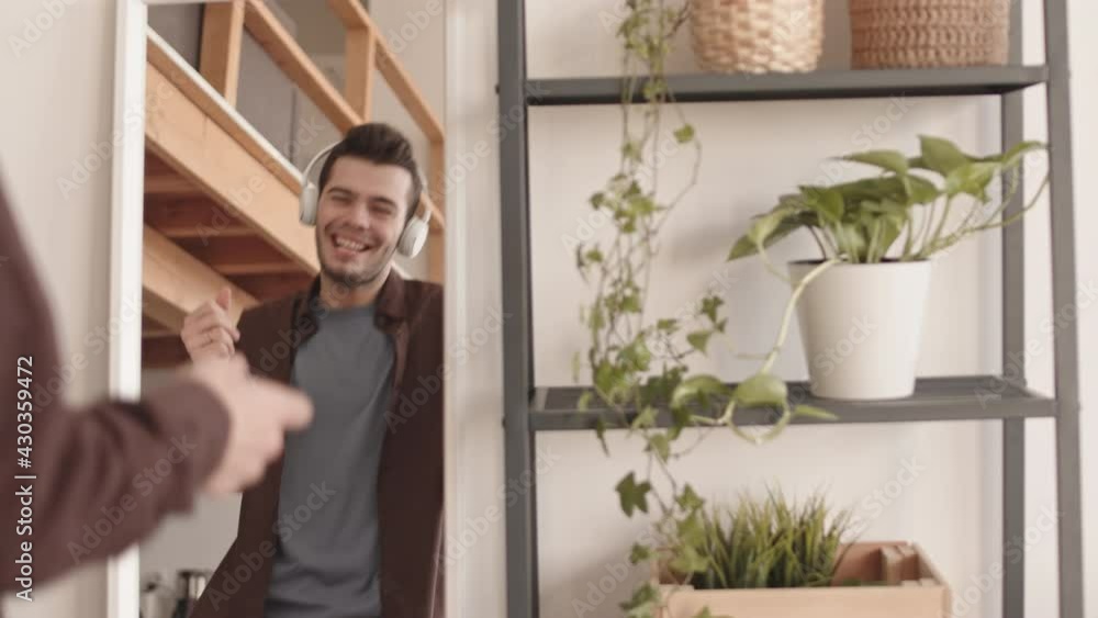 Back view of young handsome dark-haired man wearing casual clothes and headphones sanding in front of mirror and home, listening to music and dancing Back view of young handsome dark-haired man wearing casual clothes and headphones sanding in front of mirror and home, listening to music and dancing
