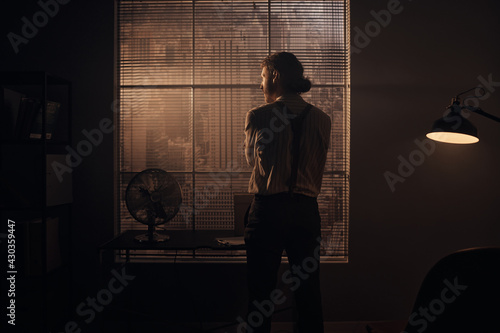 scene of a brutal young detective looking out of a window overlooking New York, he is wearing a striped shirt, classic pants with suspenders photo