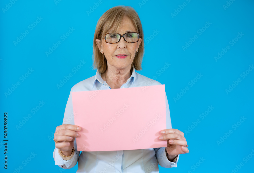 Portrait of a senior woman holding blank space paper over blue background Portrait of a senior woman holding blank space paper over blue background