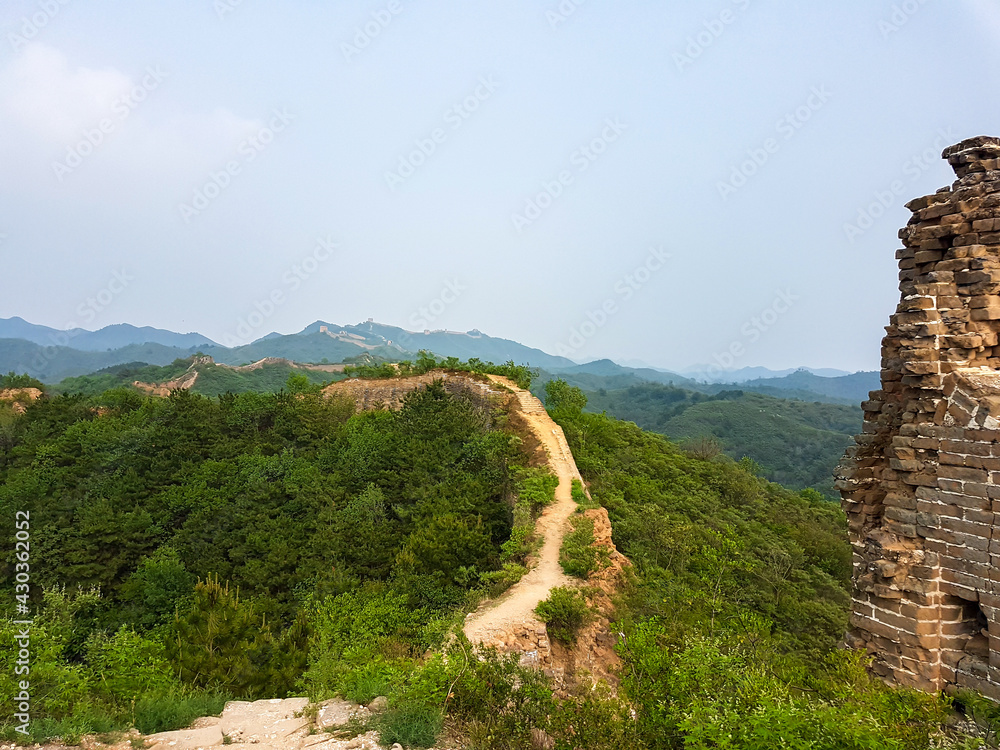 Fototapeta premium A panoramic view on an unrenewed Gubeikou part of Great Wall of China. The wall is spreading on tops of mountains. Many watchtowers on the peaks. Dense forest around it. World wonder. Tradition
