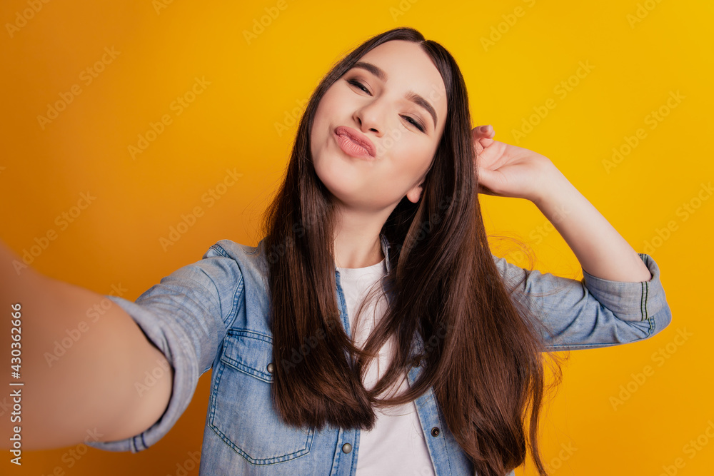 Close-up of young beautiful woman taking selfie send air kiss posing on yellow background Close-up of young beautiful woman taking selfie send air kiss posing on yellow background