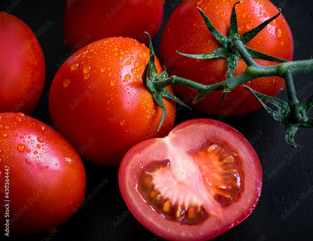 Delicious red fresh tomatoes on black background, tomato branch, half slice tomato