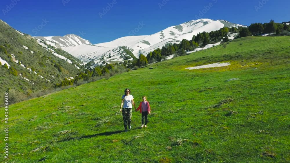Happy woman with daughter walking on grass in nature in a meadow in the mountains. Aerial view 4K. Happy woman with daughter walking on grass in nature in a meadow in the mountains. Aerial view 4K.