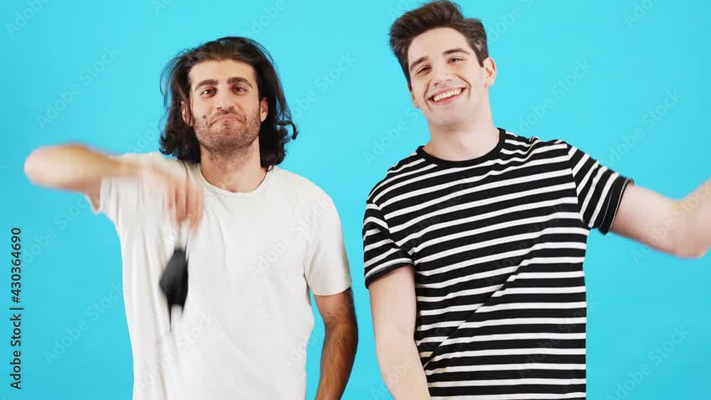 The two smiling men taking-off black disposable protective masks and shaking the hands while rejoicing in a blue studio The two smiling men taking-off black disposable protective masks and shaking the hands while rejoicing in a blue studio