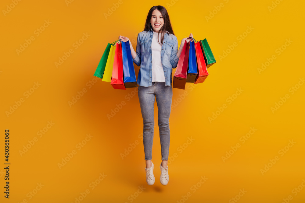 Portrait of active positive girl jumping hold shopping bargains isolated on yellow background Portrait of active positive girl jumping hold shopping bargains isolated on yellow background