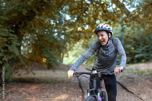 Young and happy woman in a tracksuit on a mountain bike enjoys in day ride through the park